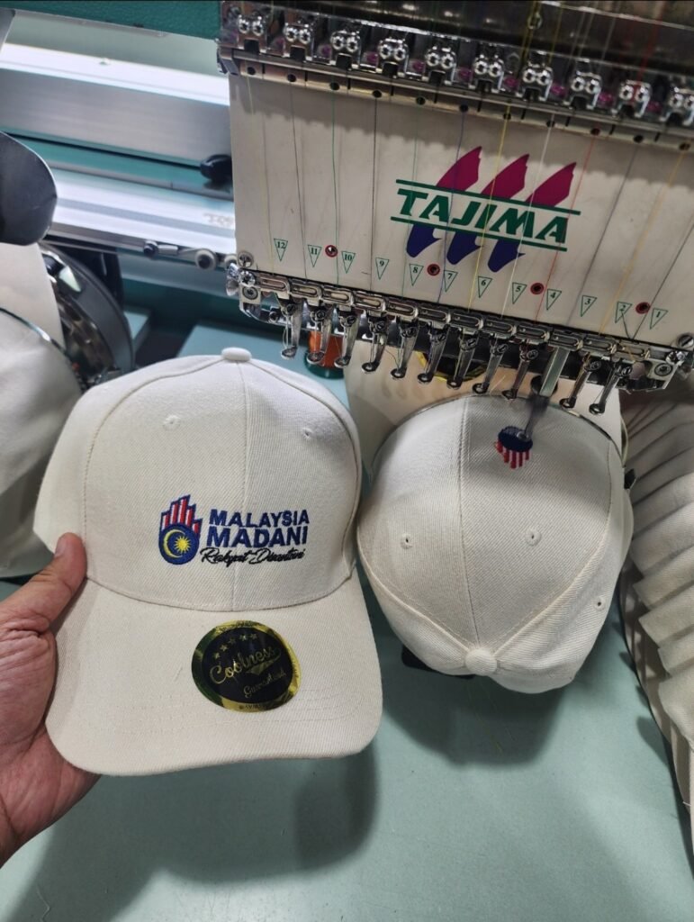 Mesin Tajima menyulam logo pada topi di kilang Saudagar Printing Malaysia